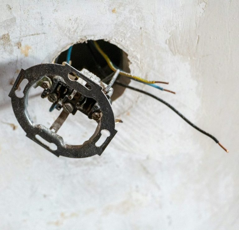 Der Unterputzrahmen einer Steckdose hängt an losen Kabeln aus der Wand.